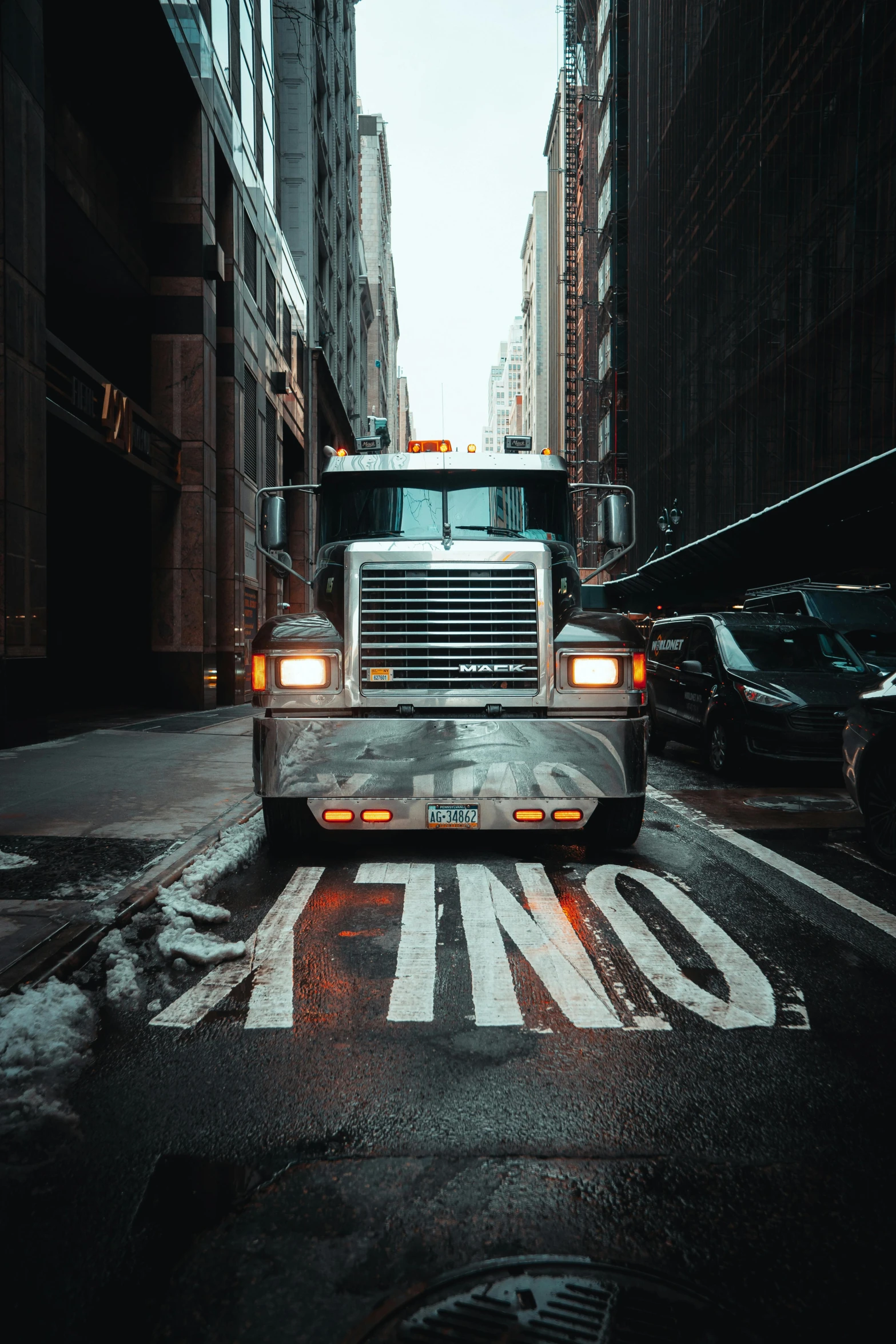 a truck driving down a street next to tall buildings, an album cover, by Dan Christensen, pexels contest winner, oily substances, 🚿🗝📝, unreal engin, wet asphalt