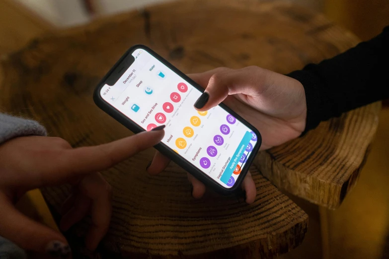 a close up of a person holding a cell phone, trending on pexels, multicoloured, on a wooden desk, app icon, rounded