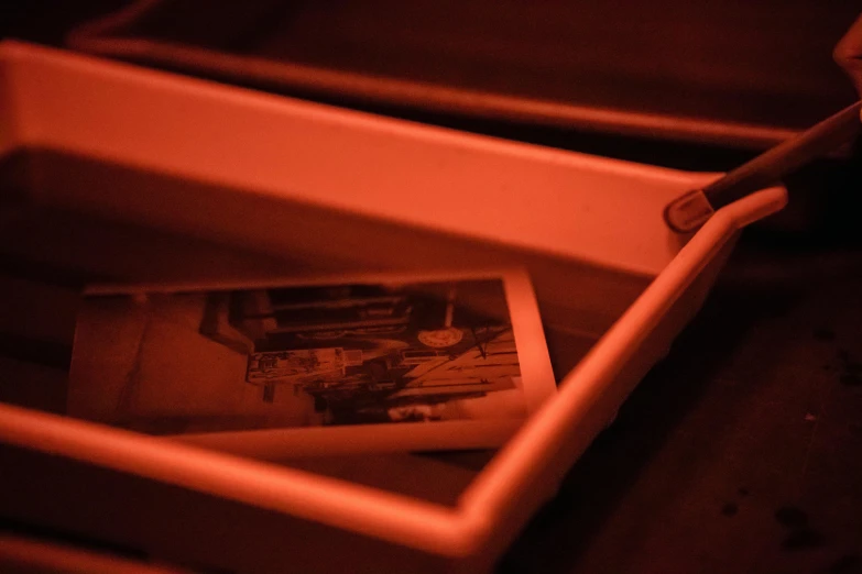 a person taking a picture of a picture in a box, a polaroid photo, by Elsa Bleda, unsplash, assemblage, lit from below with red lighting, in a red dish, sepia toned, medium close up