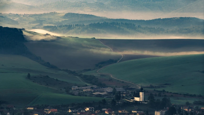 a view of a town with mountains in the background, by Wojciech Gerson, pexels contest winner, soft light misty, black forest, fields, fine art print