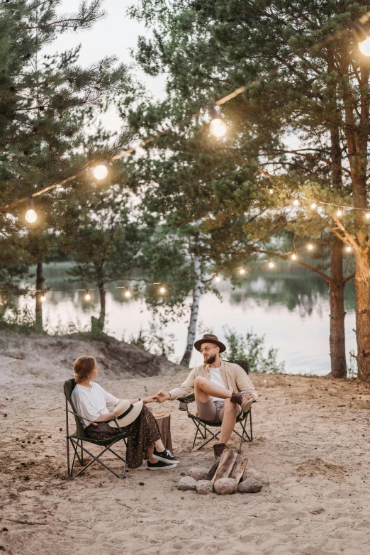 a couple of people that are sitting in chairs, by Grytė Pintukaitė, pexels contest winner, campsites, string lights, beach trees in the background, political meeting in the woods