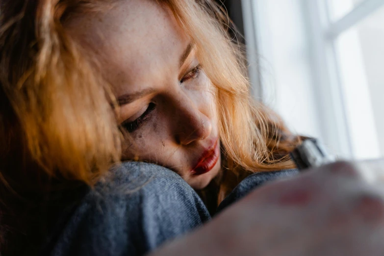 a close up of a person holding a cell phone, ginger hair with freckles, looking exhausted, looking out open window, sitting on the edge of a bed