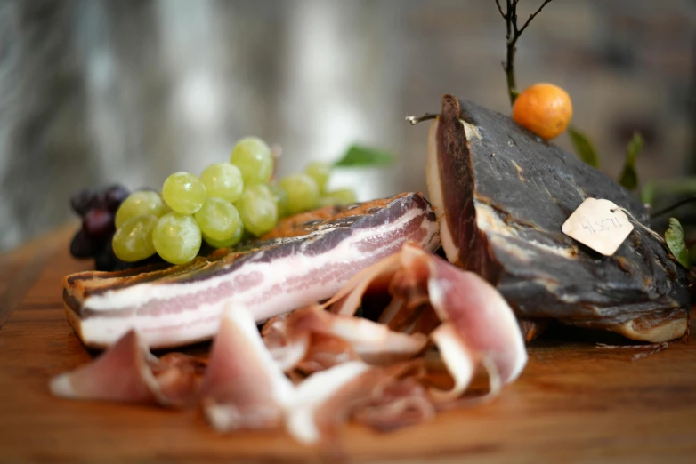 a wooden cutting board topped with meat and fruit, private press, ham, glasgow, fish in the background, charred