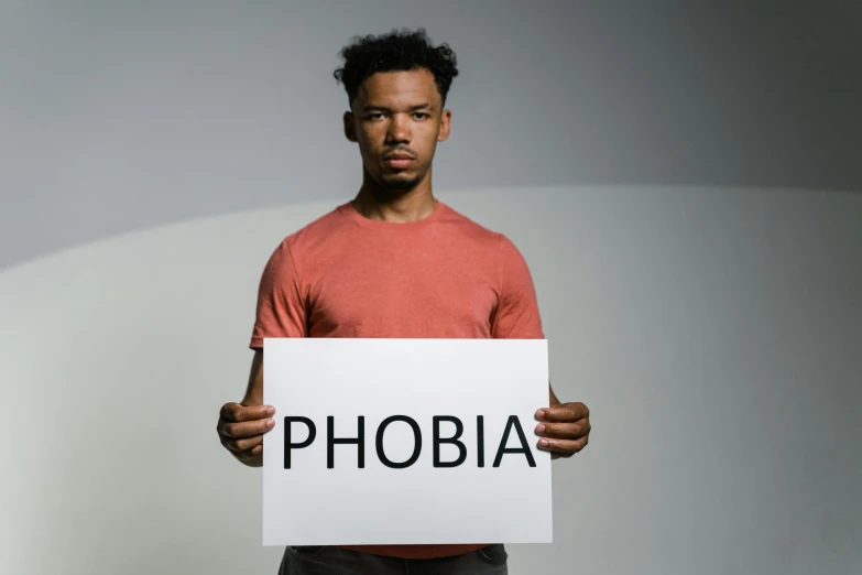 a man holding a sign that says phobia, trending on pexels, human staring blankly ahead, album art, addiction, diverse