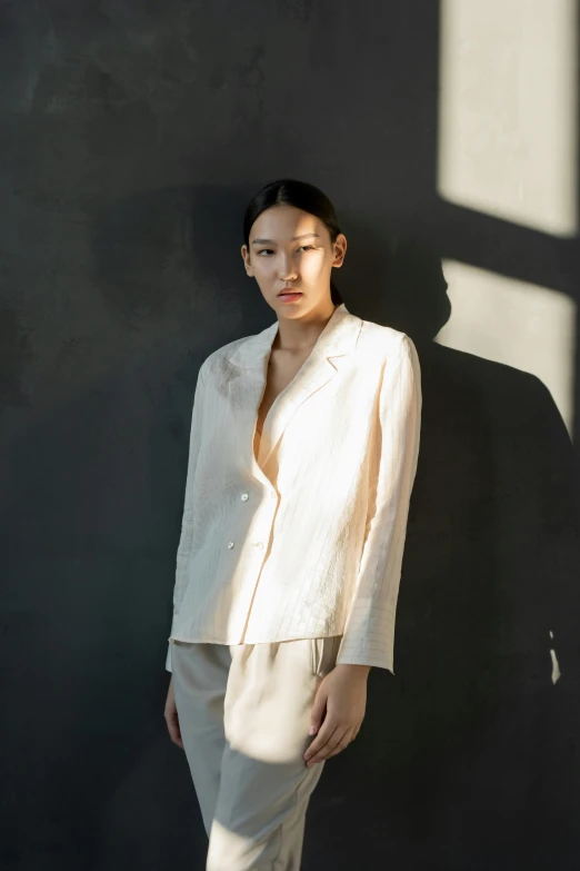 a woman standing in front of a black wall, an album cover, inspired by Li Di, unsplash, renaissance, wearing a light - pink suit, wearing a linen shirt, mariko mori, wearing white silk