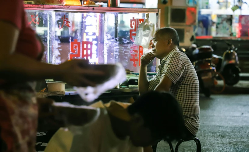 a man sitting at a table in front of a vending machine, pexels contest winner, wet market street, avatar image, early evening, thumbnail