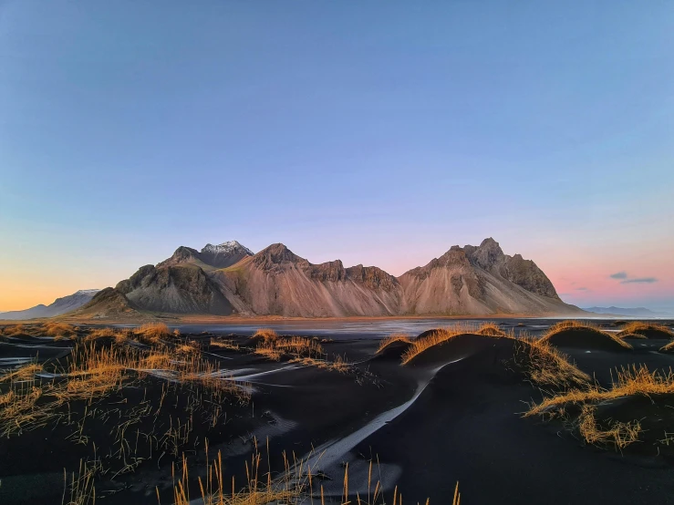 a black sand beach with mountains in the background, pexels contest winner, baroque, last light on mountain top, devils horns, dessert, taken on iphone 1 3 pro
