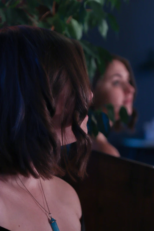 a woman sitting at a table with a cell phone in her hand, inspired by Nan Goldin, trending on pexels, view from behind mirror, girl with dark brown hair, ( ( theatrical ) ), vfx film closeup