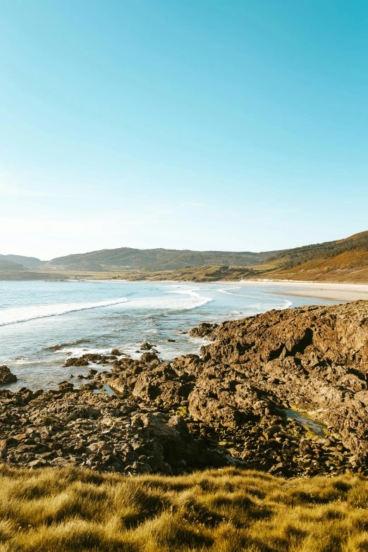 a man riding a surfboard on top of a sandy beach, hills and ocean, rock pools, vast expansive landscape, kelp