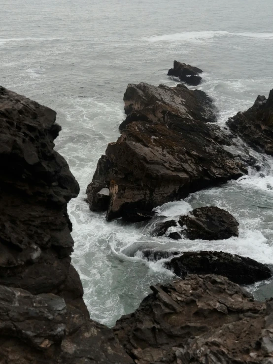 a man standing on top of a rocky cliff next to the ocean, an eerie whirlpool, overcast lighting, slide show, devil's horns