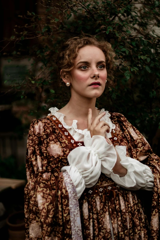 a woman in a brown dress standing in front of a tree, inspired by Thomas Stothard, unsplash, renaissance, film still of emma watson, wearing victorian rags, scrolls, concert