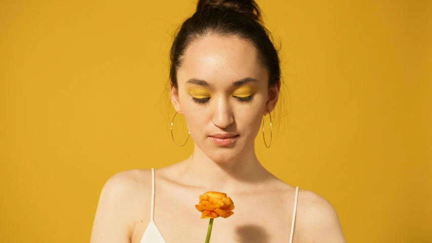 a woman holding a flower in front of her face, an album cover, inspired by Bert Stern, trending on pexels, wearing yellow croptop, portrait sophie mudd, wearing eye shadow, color photograph portrait 4k