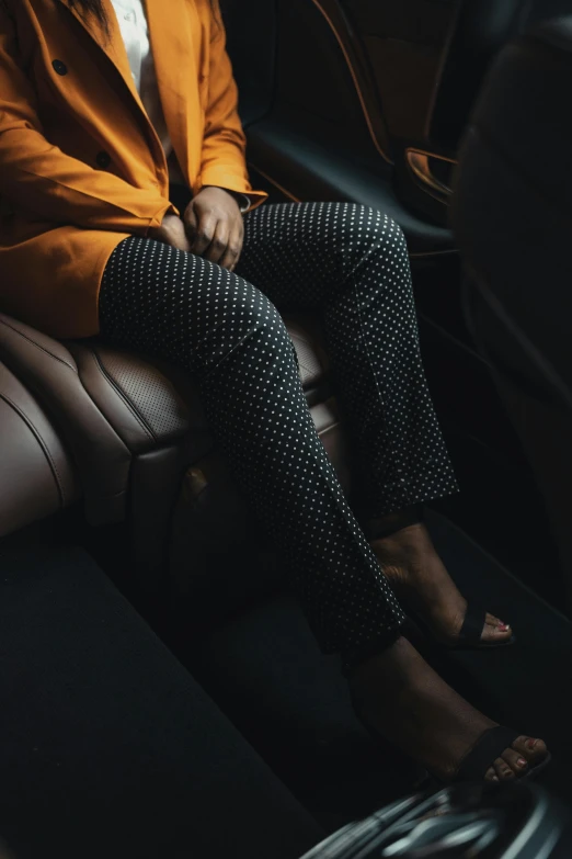 a woman sitting in the back seat of a car, trending on unsplash, renaissance, black trousers, gold suit, polkadots, dark skinned