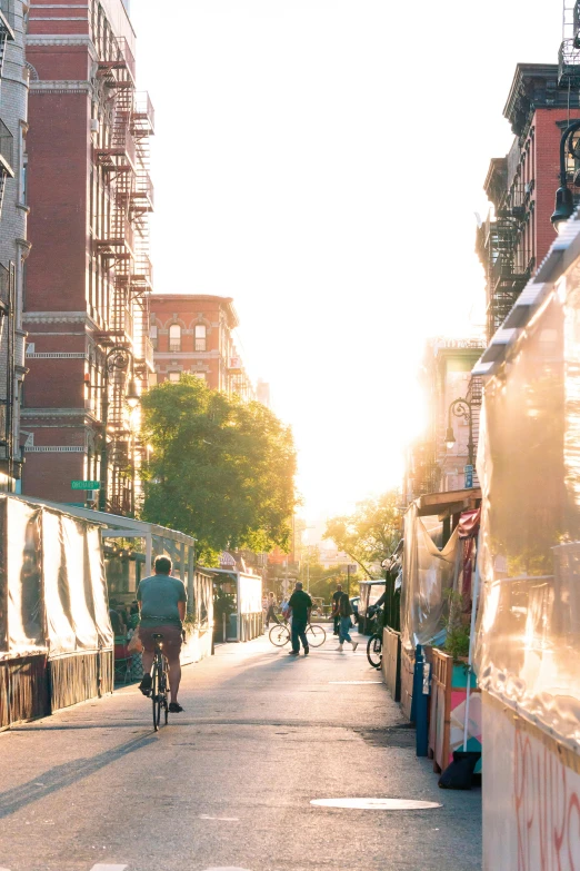 a man riding a bike down a street next to tall buildings, trending on unsplash, happening, golden hour in manhattan, shady alleys, suns, vendors