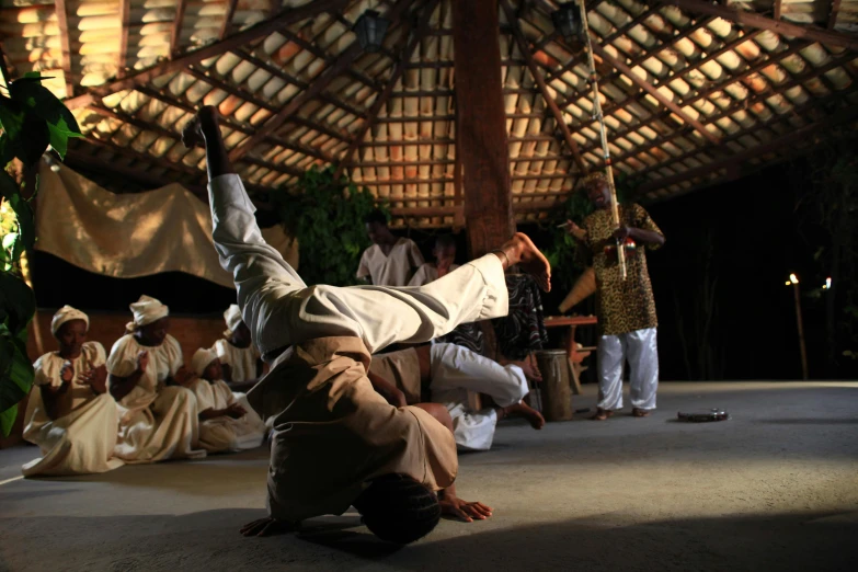 a man doing a handstand in front of a group of people, hurufiyya, african arts, in a dojo, dynamic movie still, réunion des musées nationaux