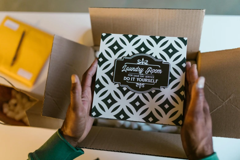 a person holding a box of doughnuts on a table, a silk screen, pexels contest winner, private press, inside its box, packaging, patterned, angled shot
