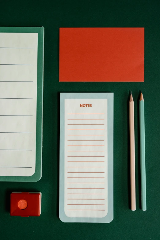 a variety of stationery items laid out on a green surface, inspired by Wes Anderson, thin red lines, on high-quality paper, grey orange, overview