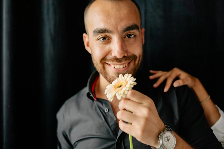 a close up of a person holding a flower, a portrait, inspired by Yehia Dessouki, pexels contest winner, with a beard and a black shirt, smiling male, professional photo-n 3, indoor picture