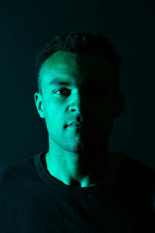 a man standing in front of a green light, an album cover, by Frank Mason, unsplash, mixed race, shadowed face, on black background, headshot profile picture
