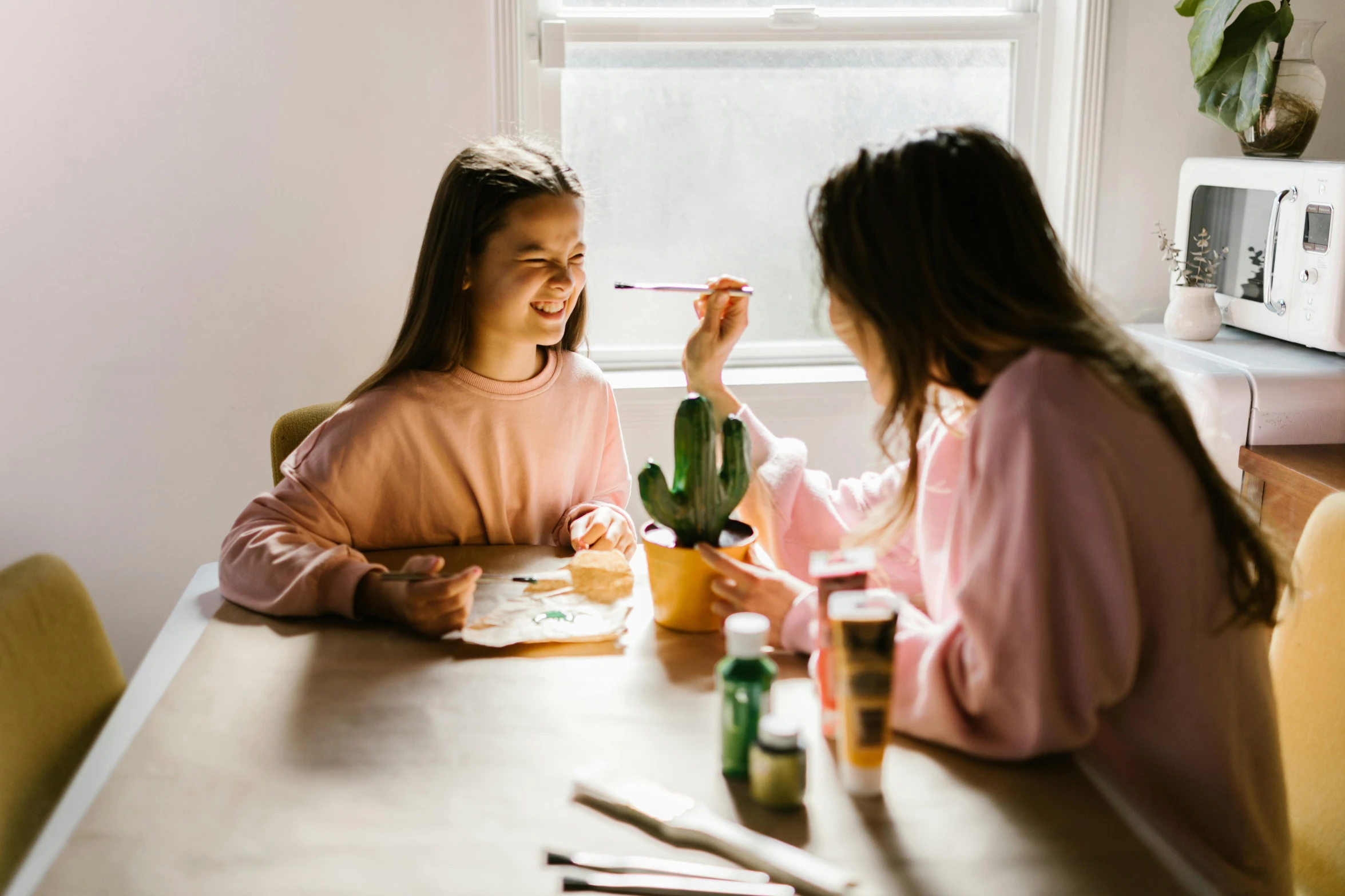 two girls sitting at a table eating food, pexels contest winner, process art, with cactus plants in the room, holding a paintbrush, sitting on a mocha-colored table, family friendly