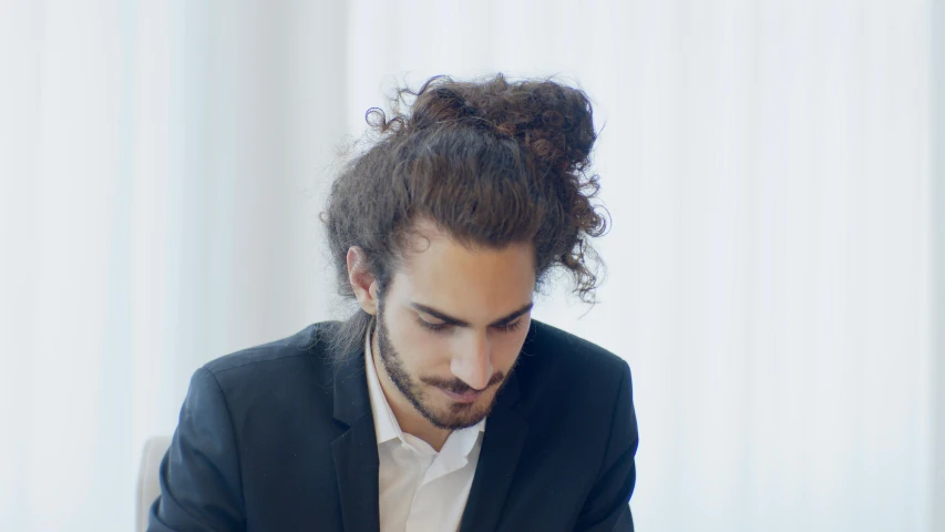 a man sitting at a table with a cell phone in his hand, an album cover, inspired by Jules Robert Auguste, pexels contest winner, renaissance, hair styled in a bun, middle eastern skin, headshot profile picture, in an office