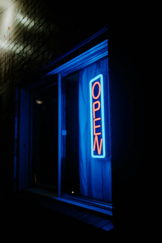 a neon sign sitting on the side of a building, a stock photo, pexels, happening, blue door, open room, (night), open vault