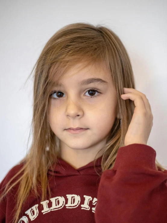 a little girl standing in front of a white wall, trending on reddit, incoherents, androgynous face, close - up studio photo, wearing hoodie, brown-blond-hair pretty face