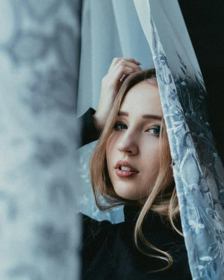 a woman that is looking out of a window, inspired by Elsa Bleda, trending on pexels, aestheticism, beautiful taissa farmiga, wrapped in a black scarf, blue and gray colors, sydney sweeney