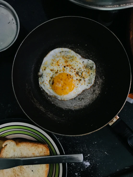 an egg frying in a frying pan next to toast, by Bernardino Mei, pexels contest winner, 🚿🗝📝, dark backdrop, instagram story, glazed