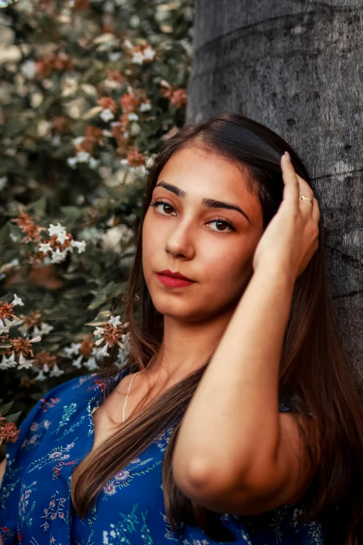 a woman in a blue dress leaning against a tree, by irakli nadar, headshot profile picture, 18 years old, olive skin color, instagram post