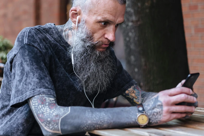 a man sitting on a bench looking at his cell phone, a tattoo, by Adam Marczyński, trending on pexels, grey trimmed beard, wood headphones hyperrealistic, photograph of a sleeve tattoo, 40 years old women