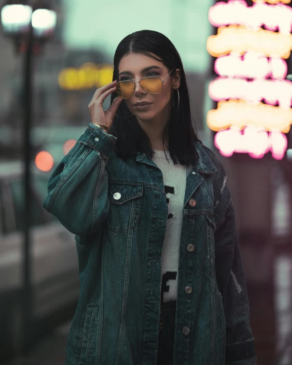 a woman standing on a city street talking on a cell phone, an album cover, inspired by Elsa Bleda, trending on pexels, yellow carrera glasses, non binary model, jean jacket, snapchat photo