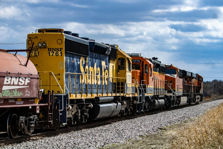 a large long train on a steel track, by Alison Geissler, unsplash, photorealism, strong blue and orange colors, golden engines, various posed, 🚿🗝📝