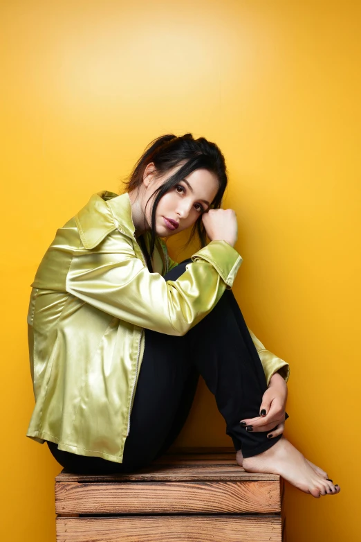 a woman sitting on top of a wooden box, an album cover, pexels, pop art, yellow clothes, charli bowater, leaning against the wall, wearing jacket