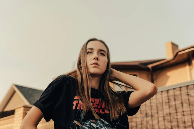 a beautiful young woman standing in front of a house, an album cover, inspired by Elsa Bleda, trending on pexels, graffiti, long hair and red shirt, wearing a black t-shirt, sydney sweeney, promotional image