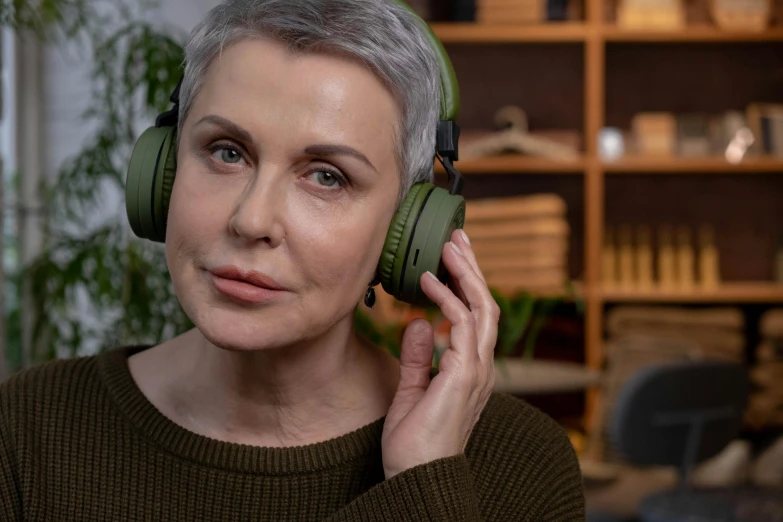 a woman with grey hair wearing green headphones, inspired by Ruth Deckard, trending on pexels, hurufiyya, middle aged, dynamic scene, wooden headphones, non-binary