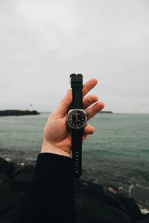 a person holding a watch in front of a body of water, reykjavik, detailed product image
