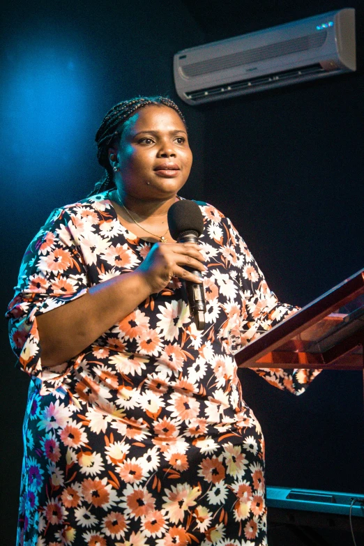 a woman standing at a podium with a microphone, by Nele Zirnite, emmanuel shiru, standing with a black background, church, plus-sized