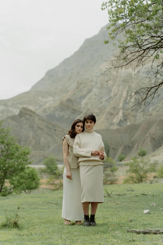 two women standing next to each other in a field, by Muggur, cliffs, off - white collection, reza afshar, couples portrait