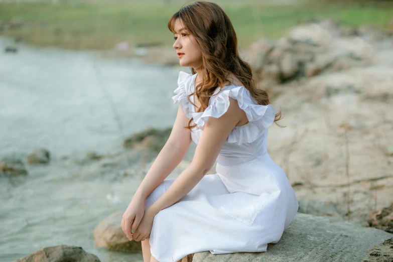 a woman sitting on a rock near a body of water, inspired by Kim Du-ryang, pexels contest winner, renaissance, pretty white dress, girl cute-fine-face, attractive brown hair woman, frilly outfit