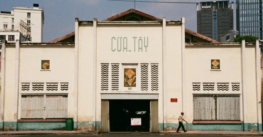 a building with a man walking in front of it, inspired by Cui Bai, temporary art, tafy, from the front, old signs, colonial