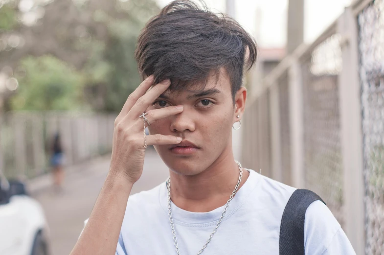 a young man standing in front of a fence talking on a cell phone, an album cover, inspired by Jorge Jacinto, trending on pexels, realism, young cute wan asian face, undercut hairstyle, hands on face, headshot profile picture