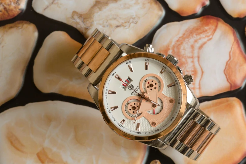 a watch sitting on top of a pile of rocks, on a wooden table, ivory and copper, daytoner, thumbnail