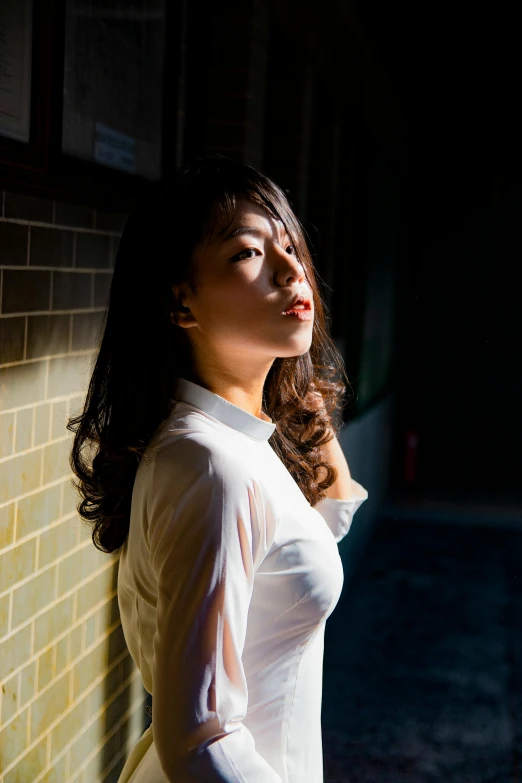 a woman standing in front of a brick wall, inspired by Zheng Xie, pexels contest winner, backlit portrait, wearing a white shirt, large)}], asian woman