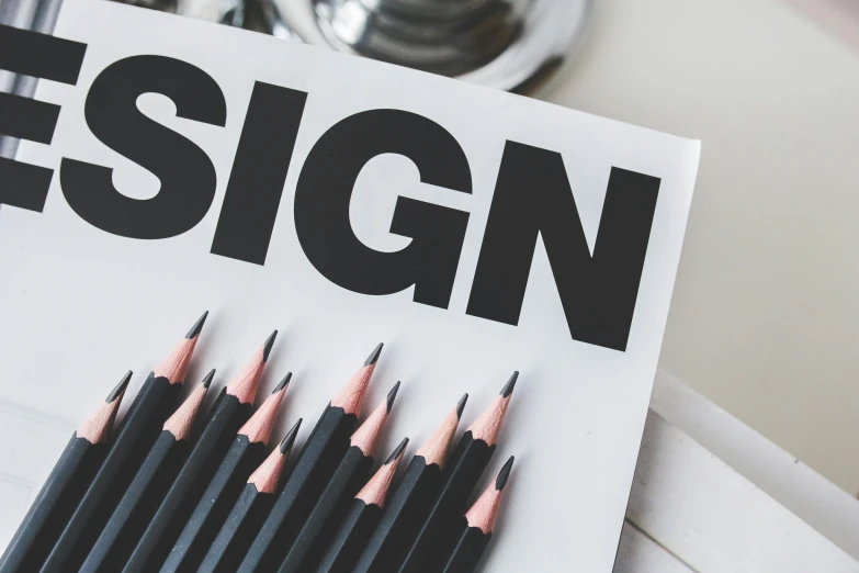 a bunch of pencils sitting on top of a piece of paper, a poster, trending on pexels, international typographic style, signs, vinyl on glazing, black design, user interface design