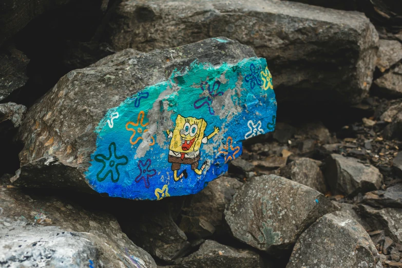 a rock sitting on top of a pile of rocks, a cave painting, by artist, unsplash, graffiti, spongebob squarepants, blue, cardboard, advertising photo