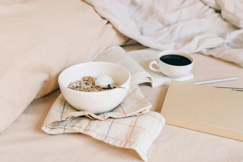 a bowl of cereal and a cup of coffee on a bed, by Emma Andijewska, pexels contest winner, light beige pillows, black, small, thumbnail