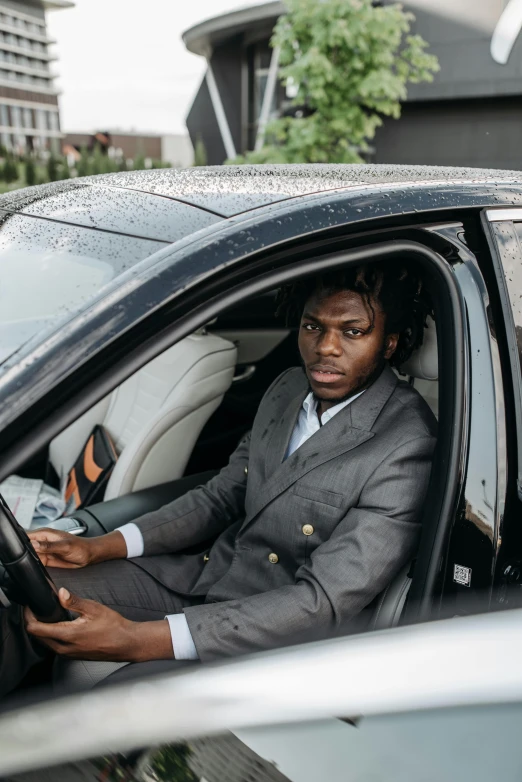 a man in a suit sitting in a car, dark skin tone, gen z, performance, square