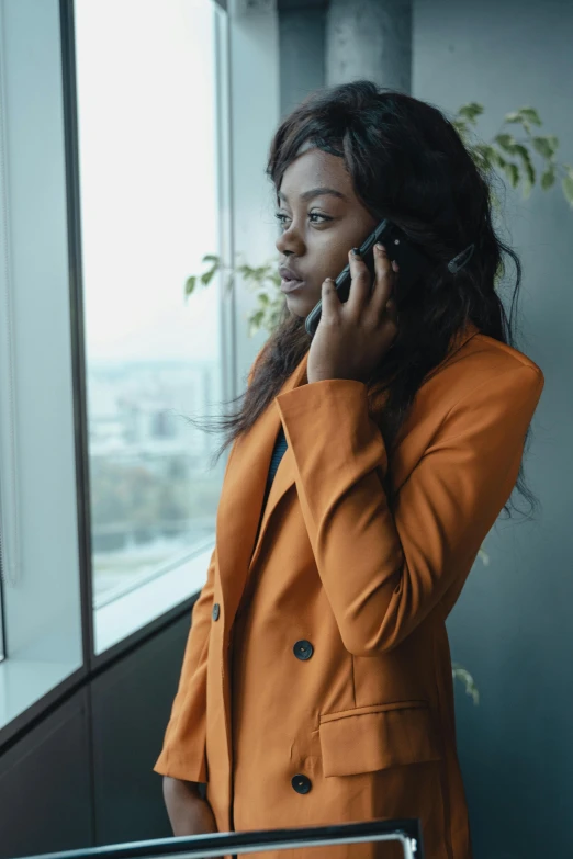 a woman in an orange jacket talking on a cell phone, trending on pexels, renaissance, woman in black business suit, ( ( dark skin ) ), alessio albi, office clothes