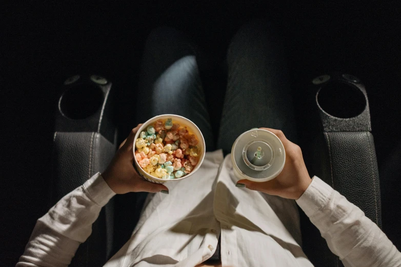 a man sitting in a chair holding a bowl of food, trending on unsplash, hyperrealism, sitting in a movie theater, high - angle view, medium shot of two characters, bowl filled with food